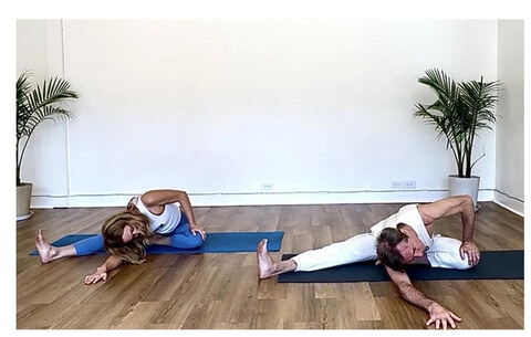 Two students fold forward over wide legs in a deep floor stretch.