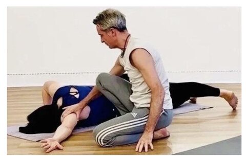 Wayne works both hands into a client's shoulder during a supine twist treatment.